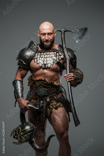 Shot of nordic barbarian with muscular build holding hatchet and helmet with horns