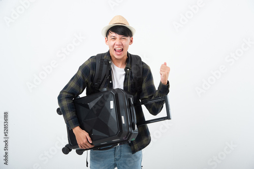 Happy Asian young man traveler holding carrying travel luggage doing winner gesture isolated on white background studio. Lifestyle traveling