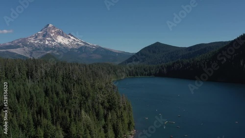 Aerial orbit and reveal shot of Mt. Hood and many boats and kayaks on water at Lost Lake during the peak of summer season in Oregon.