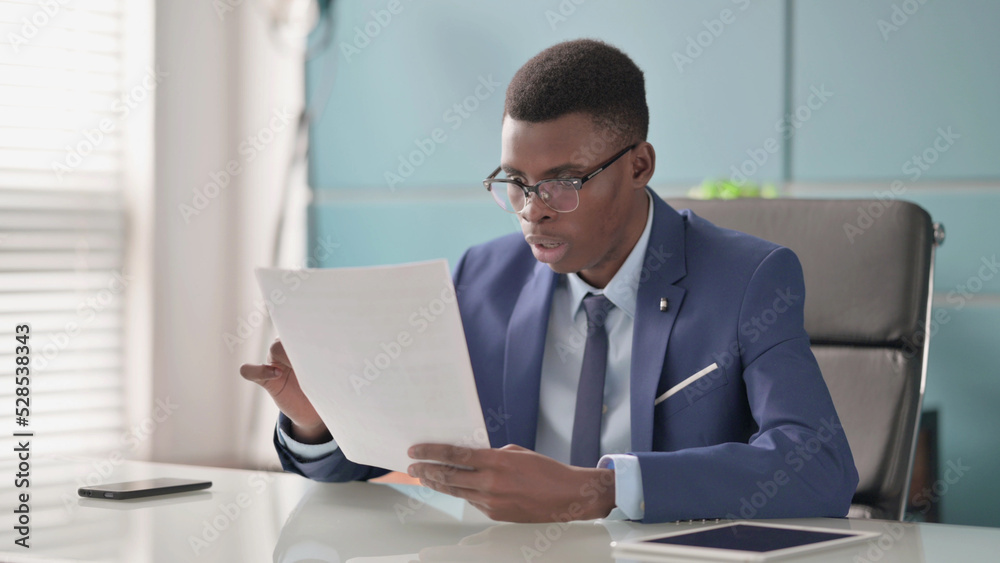 Young African Businessman Upset while Reading Documents in Office Young African Businessman Upset while Reading Documents in Office