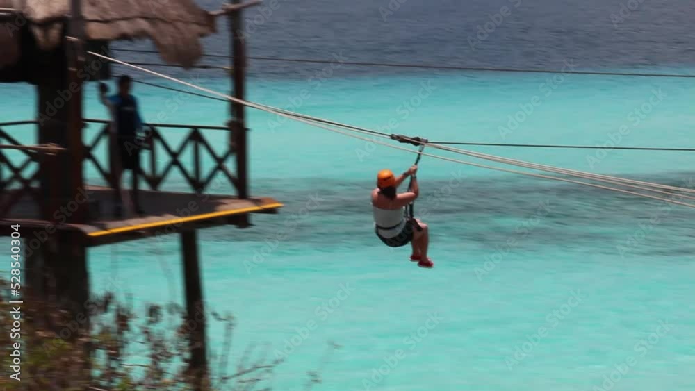 Anonymous woman on zipline over tourquoise water of Caribbean Sea in Isla Mujeres, Mexico. Summer vacation, adventure activity in tropical destination concept