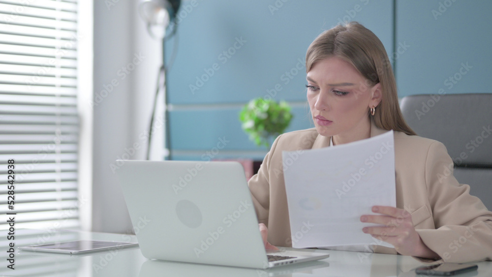 Businesswoman Reading Reports while Using Laptop