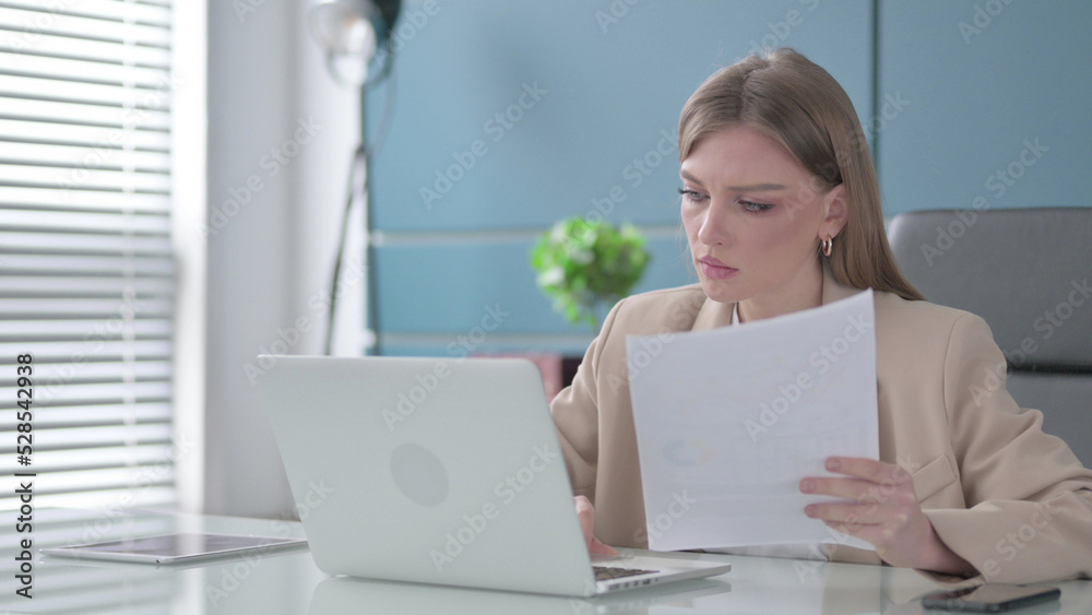 Businesswoman Reading Reports while Using Laptop Businesswoman Reading Reports while Using Laptop