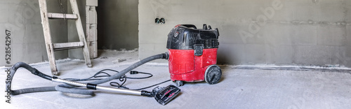 Red industrial vacuum cleaner at new house construction site, wide banner photo, space for text right side