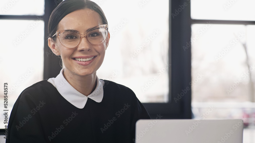 happy businesswoman in eyeglasses looking at camera near blurred laptop. happy businesswoman in eyeglasses looking at camera near blurred laptop.
