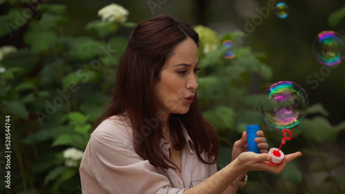Woman blowing soap bubble in summer park.