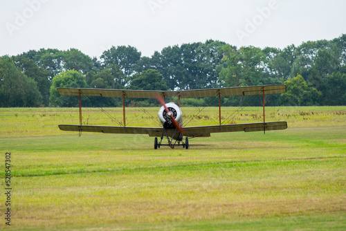 Vintage biplane prepares for takeoff at an open airfield surrounded by lush greenery on a clear day photo