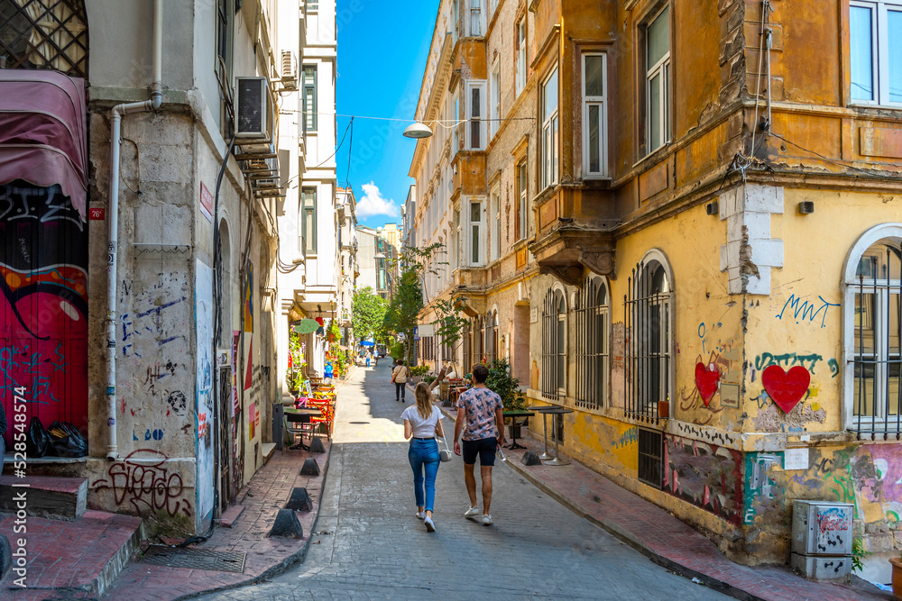 A young couple walks up a colorful hillside alley in the Karakoy Galata district of Istanbul, Turkey.