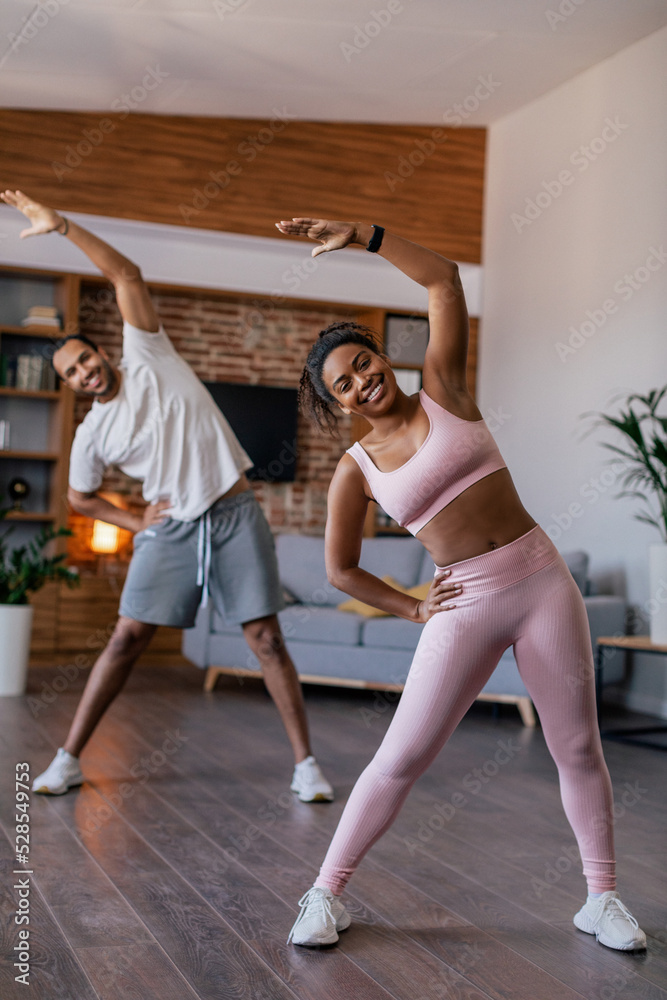 Obraz premium Cheerful young african american husband and wife in sportswear doing stretching or warm up exercises