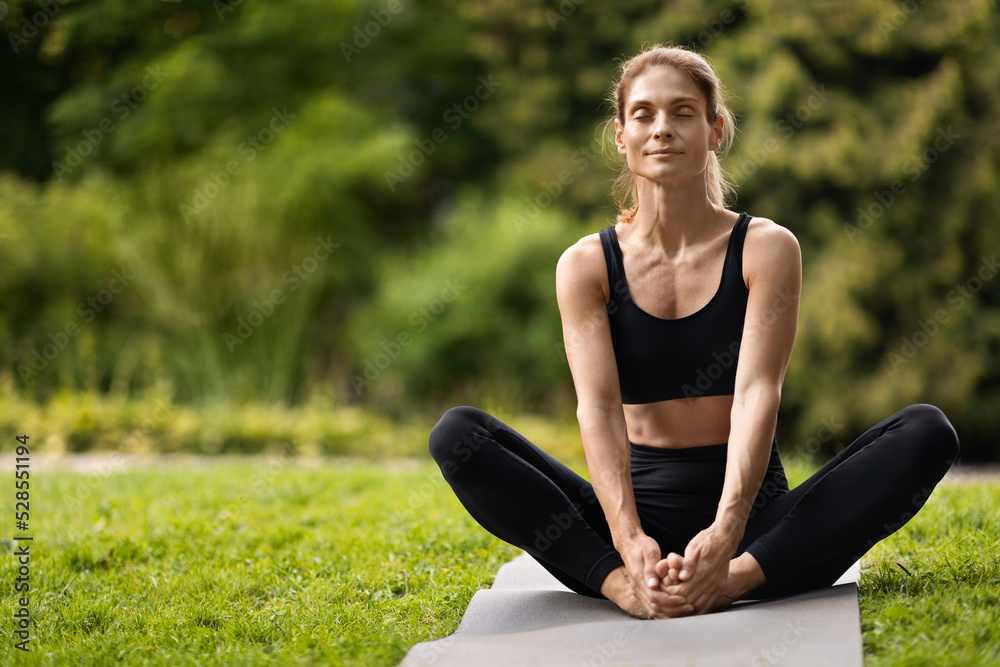 Fototapeta premium Peaceful slender woman stretching on fitness mat outdoors