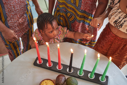 Above view of African little girl lighting candles at table together with her family in national costumes to celebrate holiday photo