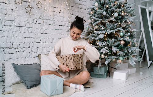 Woman opening gift near Christmas tree at home photo