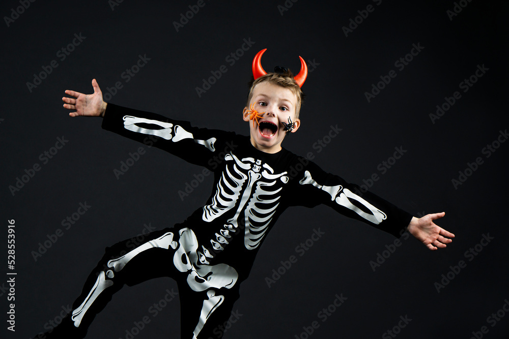 smiling screaming boy in black suit with skeleton bones and red devil horns with spider face jumping over and having fun on black background with copy space. smiling screaming boy in black suit with skeleton bones and red devil horns with spider face jumping over and having fun on black background with copy space.