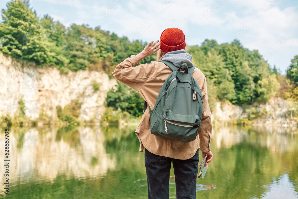 Back view of stylish hipster woman wearing backpack, red hat looking at mountain lake view while relaxing in nature. Relax time on holiday concept travel Back view of stylish hipster woman wearing backpack, red hat looking at mountain lake view while relaxing in nature. Relax time on holiday concept travel