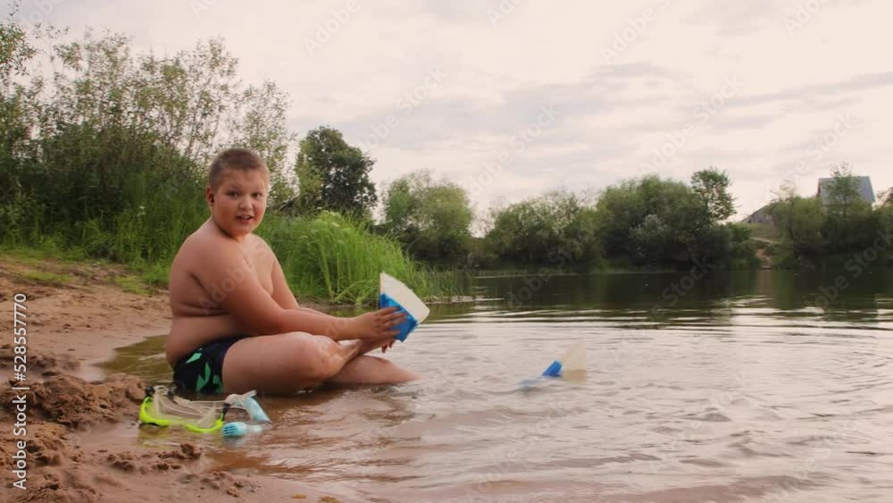 The boy sits on the shore of the lake and puts flippers on his feet. A ...