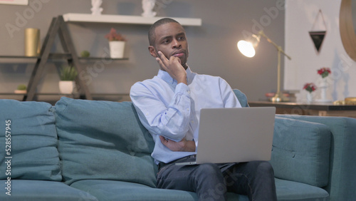 African Man with Laptop Thinking on Sofa