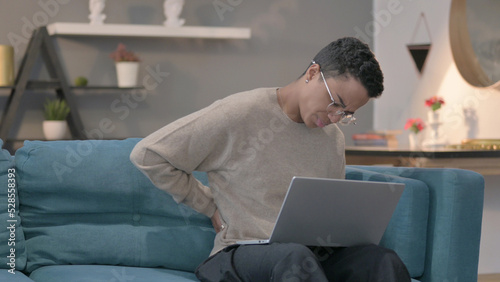 African Woman with Laptop having Back Pain on Sofa