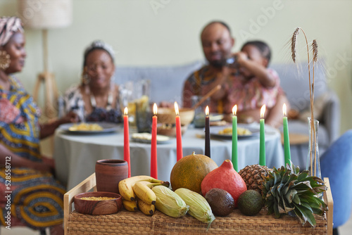 Close-up of traditional decoration with candles and exotic fruits for Kwanzaa celebration with family having dinner in background photo