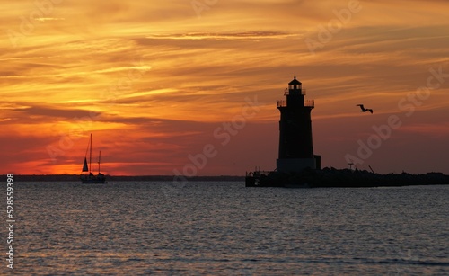 Silhouette of lighthouse and a yacht during sunset near Cape Henlopen State Park, Lewes, DE photo