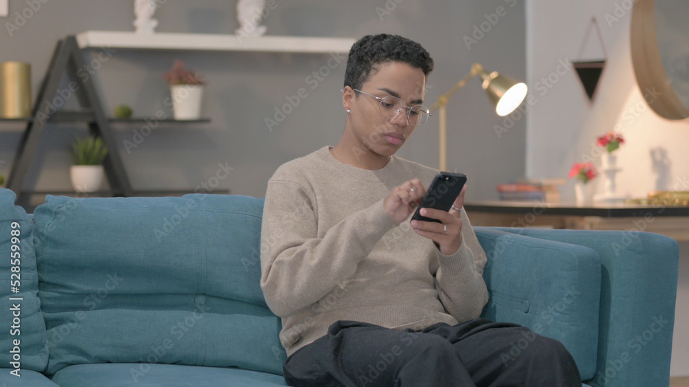 African Woman using Smartphone while Sitting on Sofa