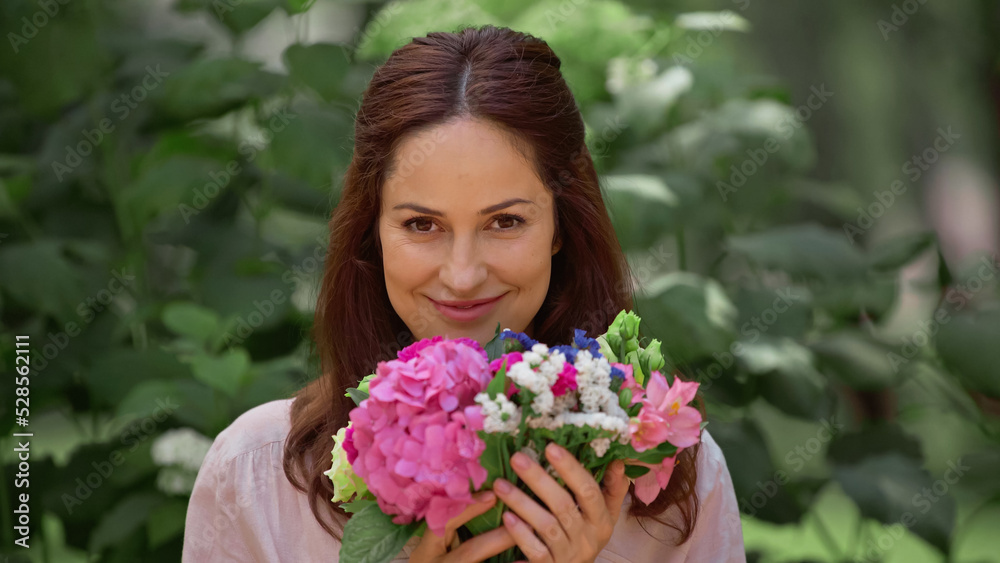 Cheerful brunette woman looking at camera and holding flowers in park. Cheerful brunette woman looking at camera and holding flowers in park.