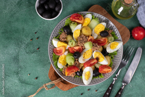 French salad Nicoise with canned tuna, boiled potatoes, egg, black olives, cucumbers, tomatoes and lettuce on gray plate, Copy space