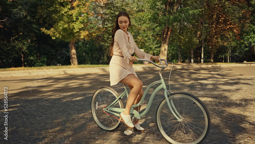 Smiling woman in dress riding bicycle in summer park.