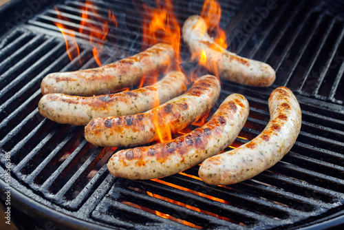 Rohe grobe gegrillte Allgäuer Bratwurst angeboten als close-up auf einem Holzkohlegrill mit Feuer und Rauch photo