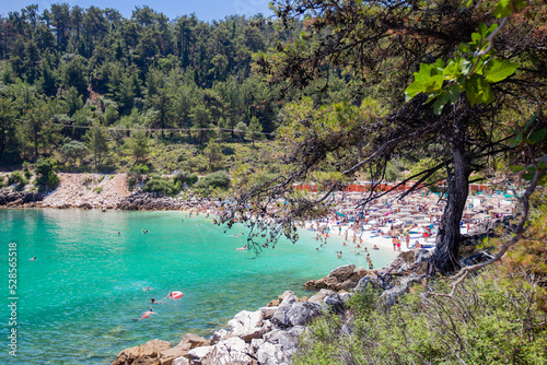 View on Marble Beach with tourists, most famous beach on Thasos, Greece. Turquoise clear sea water. Pine trees surround the beach. Holiday and travel concept.
