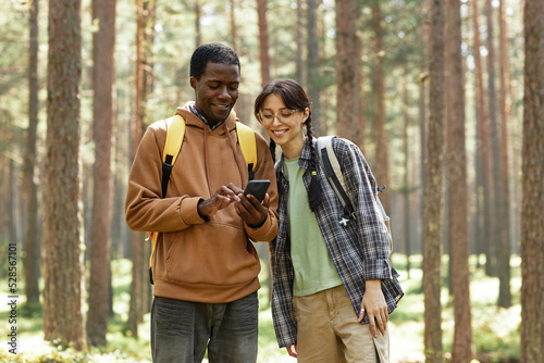 Multiethnic young couple using mobile phone while standing in the forest during hiking © Seventyfour