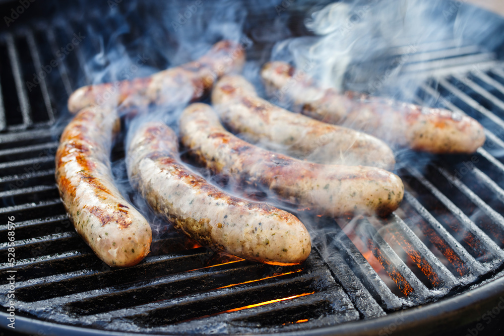 Gegrillte Allgäuer Bratwurst angeboten als close-up auf einem Holzkohlegrill mit Feuer und Rauch Gegrillte Allgäuer Bratwurst angeboten als close-up auf einem Holzkohlegrill mit Feuer und Rauch