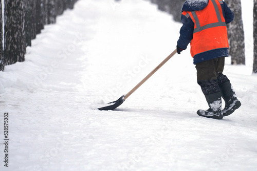 An employee of the municipal service cleans snow from the pedestrian walkway of the alley with a shovel after a snowfall. Selective focus.