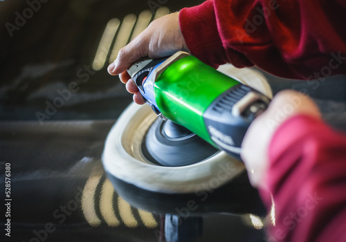 Car detailing - hands with an orbital polishing machine in an auto repair shop. Selective focus. A man polishes a car with a close-up grinder. 