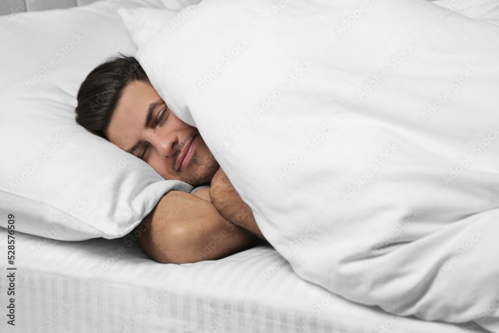 Handsome man sleeping under soft blanket in bed at home