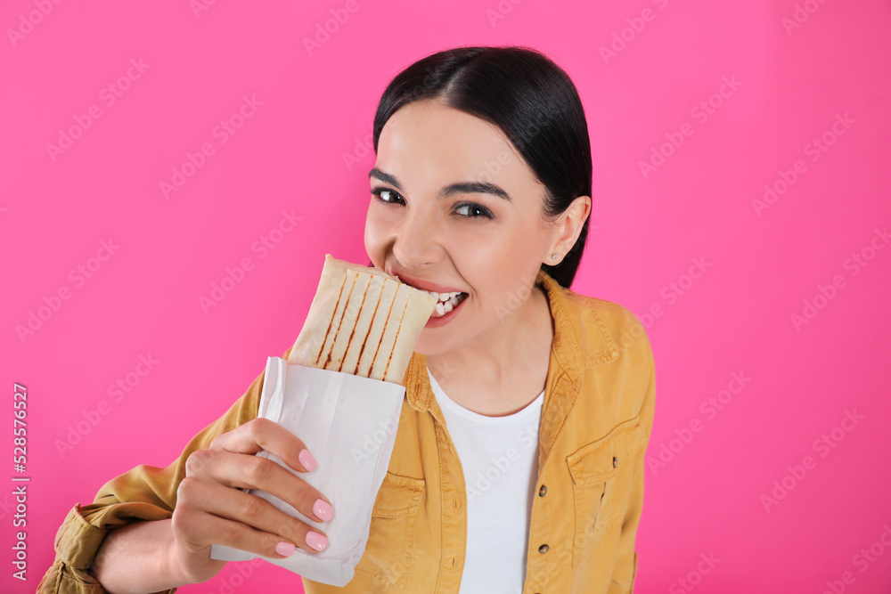 Young woman eating delicious shawarma on pink background Young woman eating delicious shawarma on pink background