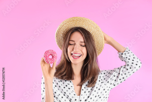 Beautiful young woman wearing stylish hat with donut on light pink background