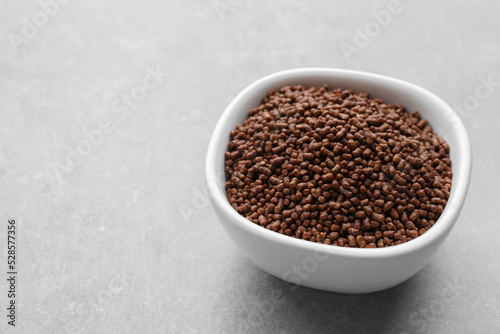 Buckwheat tea granules in bowl on light grey table. Space for text