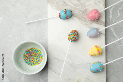 Egg shaped cake pops for Easter celebration on grey marble table, flat lay