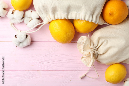 Fototapeta Naklejka Na Ścianę i Meble -  Cotton eco bags with citrus fruits on pink wooden table, flat lay