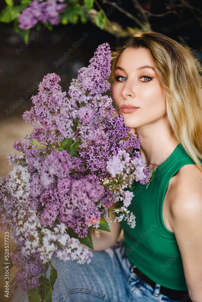 Fototapeta premium a blonde woman in a green top and jeans with lilac flowers. 