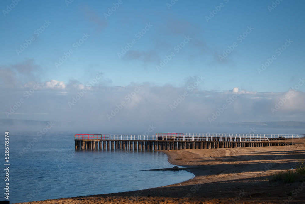 View of the beach with concrete piers and dissipating fog over the river in the early morning.