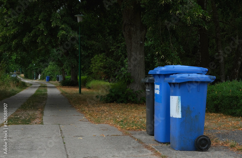 Blue and black trash bins lined up for collection in a small village in Germany. Residual waste and recycling of paper and cardboard.
