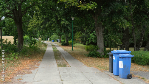 Blue and black trash bins lined up for collection in a small village in Germany. Residual waste and recycling of paper and cardboard.