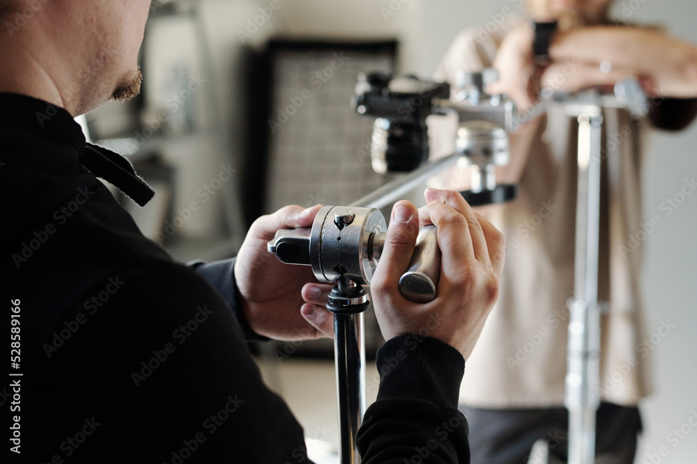 Hands of young photographer or assistant adjusting metallic slider for steadicam while preparing for shooting new commercial Hands of young photographer or assistant adjusting metallic slider for steadicam while preparing for shooting new commercial