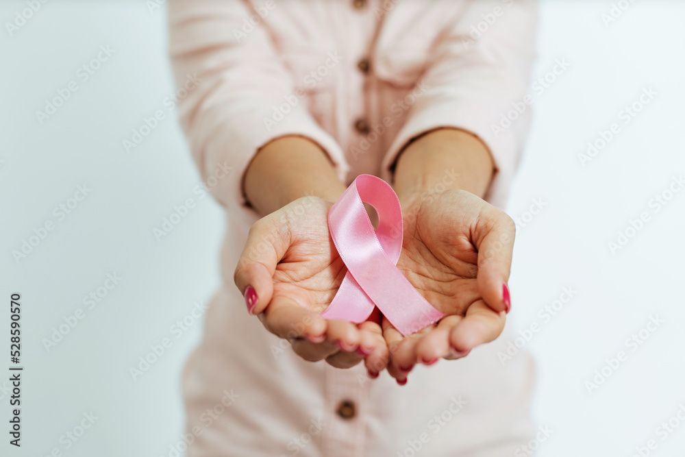 Close-up of woman's hands holding pink ribbon. Breast cancer awareness concept - obrazy, fototapety, plakaty 