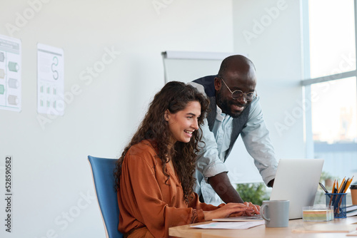 Two young creative designers working over new project in front of laptop while smiling businesswoman entering points and ideas photo