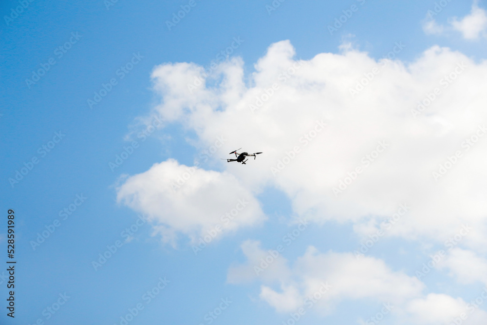 Defocus war drone. Drone flying in a blue sky. The black army unmanned aerial vehicle with four propellers and blades is on the blue sky background. Out of focus Defocus war drone. Drone flying in a blue sky. The black army unmanned aerial vehicle with four propellers and blades is on the blue sky background. Out of focus