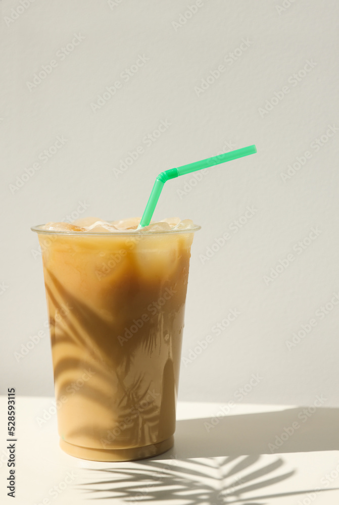 Plastic takeaway cup of delicious iced coffee on white table under sunlight Plastic takeaway cup of delicious iced coffee on white table under sunlight