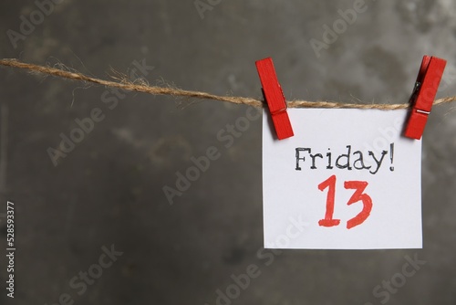 Paper note with phrase Friday! 13 hanging on twine against grey background, space for text. Bad luck superstition photo