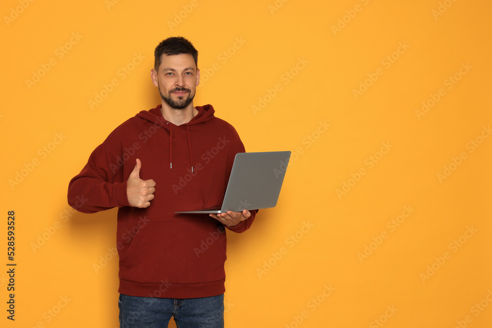 Handsome man with laptop showing thumbs up on orange background. Space for text Handsome man with laptop showing thumbs up on orange background. Space for text
